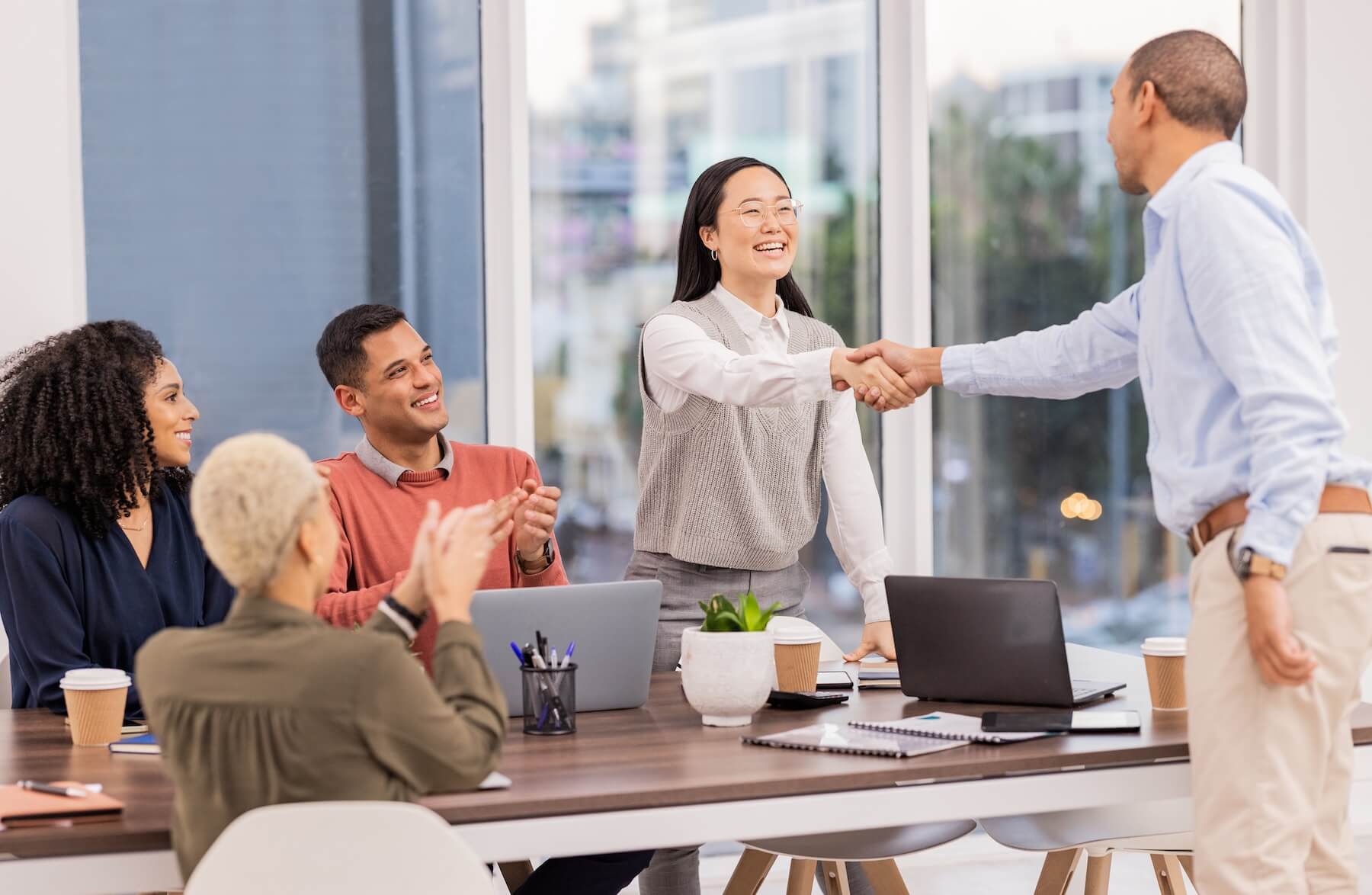 Equipo de trabajo dándose la mano alrededor de una mesa de reuniones en una oficina luminosa
